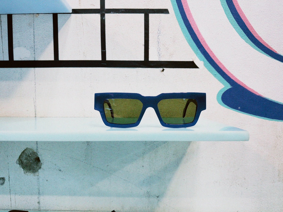 Common Ground Sonnenbrille mit blauer eckiger Fassung und grünen Gläsern
