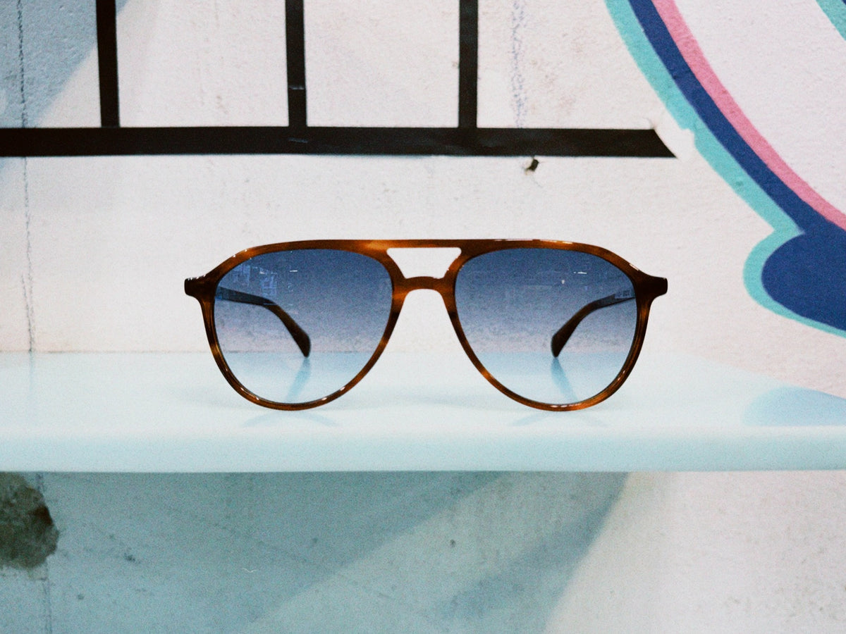Ross & Brown Sonnenbrille mit brauner Fassung und blauen Gläsern auf einer hellen Ablage